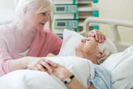 Elderly woman caring for elderly man in hospital