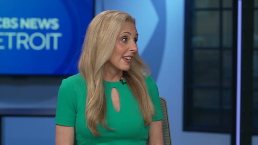 A blonde woman in a green top smiles, speaking in a news studio. The backdrop reads 'CBS NEWS DETROIT'.
